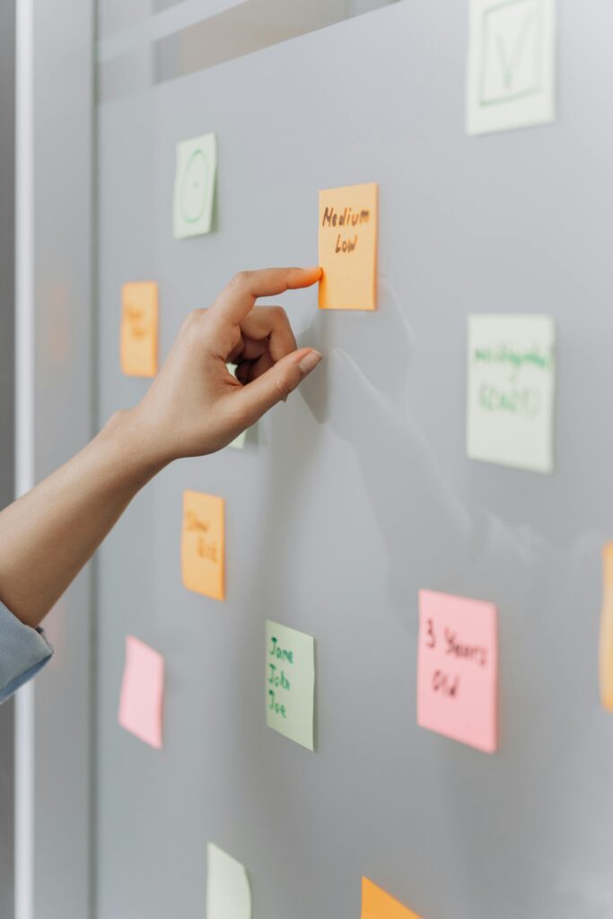 Person organizing colorful sticky notes on a glass wall in an office setting.